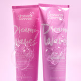 Two pink bottles of Umberto Giannini Dreamy Waves hair care products on a light purple background